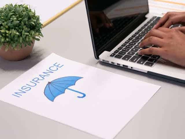 hand typing on a laptop with with an illustration of insurance on paper by the side
